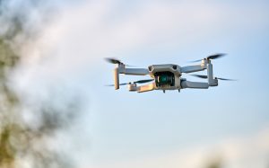 A small, modern camera drone in mid-flight against a blurred outdoor background