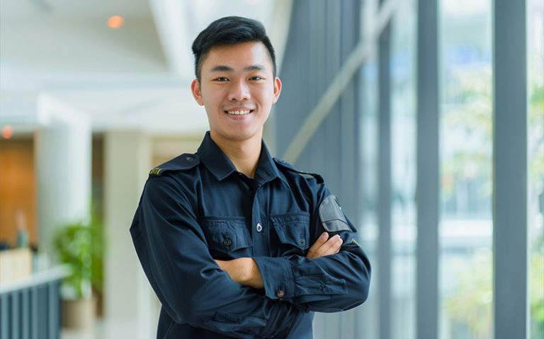 A young, confident security professional in uniform standing in a modern office building