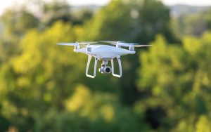 White drone hovering mid-air against a blurred green background